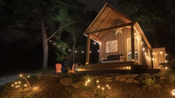 A wooden cabin with a porch, surrounded by trees and illuminated by string lights. - STARWOOD - PET FRIENDLY! - OFF GRID - ROMANTIC - ON WINE TRAIL (Hammondsport)