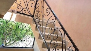 Escadaria em espiral com grades de metal preto ornamentadas e um detalhe decorativo verde no topo.