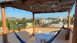 Terraço no telhado com uma rede, cadeiras de plástico brancas e uma mesa.