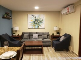 A living room with a grey sofa, two armchairs, a coffee table, and a painting on the wall.