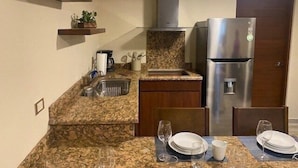 Uma cozinha compacta com bancadas de granito, geladeira de aço inoxidável e uma pia.