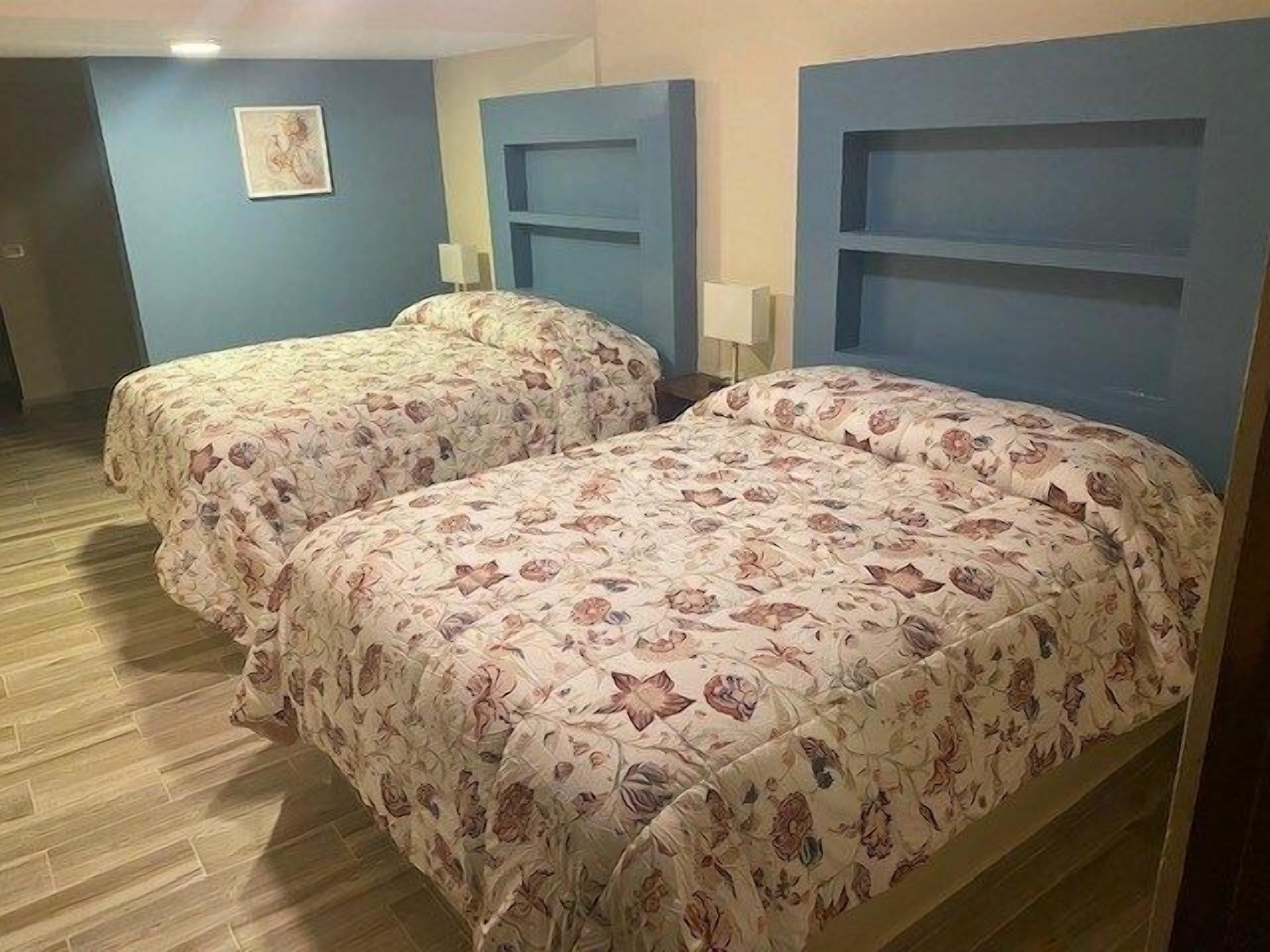 A hotel room with two beds, each with floral-patterned bedding and headboards.
