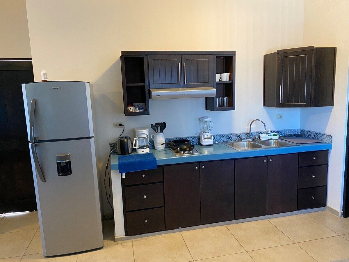 A compact kitchen with a refrigerator, a coffee maker, a blender, and a sink.