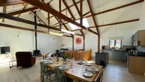 A spacious dining area with a high ceiling and exposed beams, a kitchen with modern appliances, and a cozy seating area with a fireplace. - Tawny Cottage pet friendly, barn conversion, quiet farm location, nr Dartmouth. (Dartmouth)