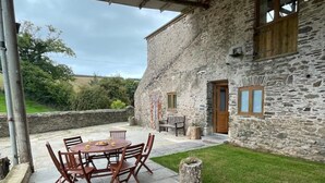 A stone building with a patio area featuring a round table and chairs, a wooden bench, and a small tree stump. - Tawny Cottage pet friendly, barn conversion, quiet farm location, nr Dartmouth. (Dartmouth)