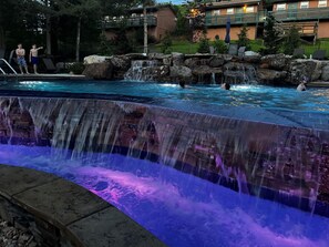 A swimming pool with a waterfall feature and a view of a building with outdoor seating. - The Bavarian Resort (Branson)
