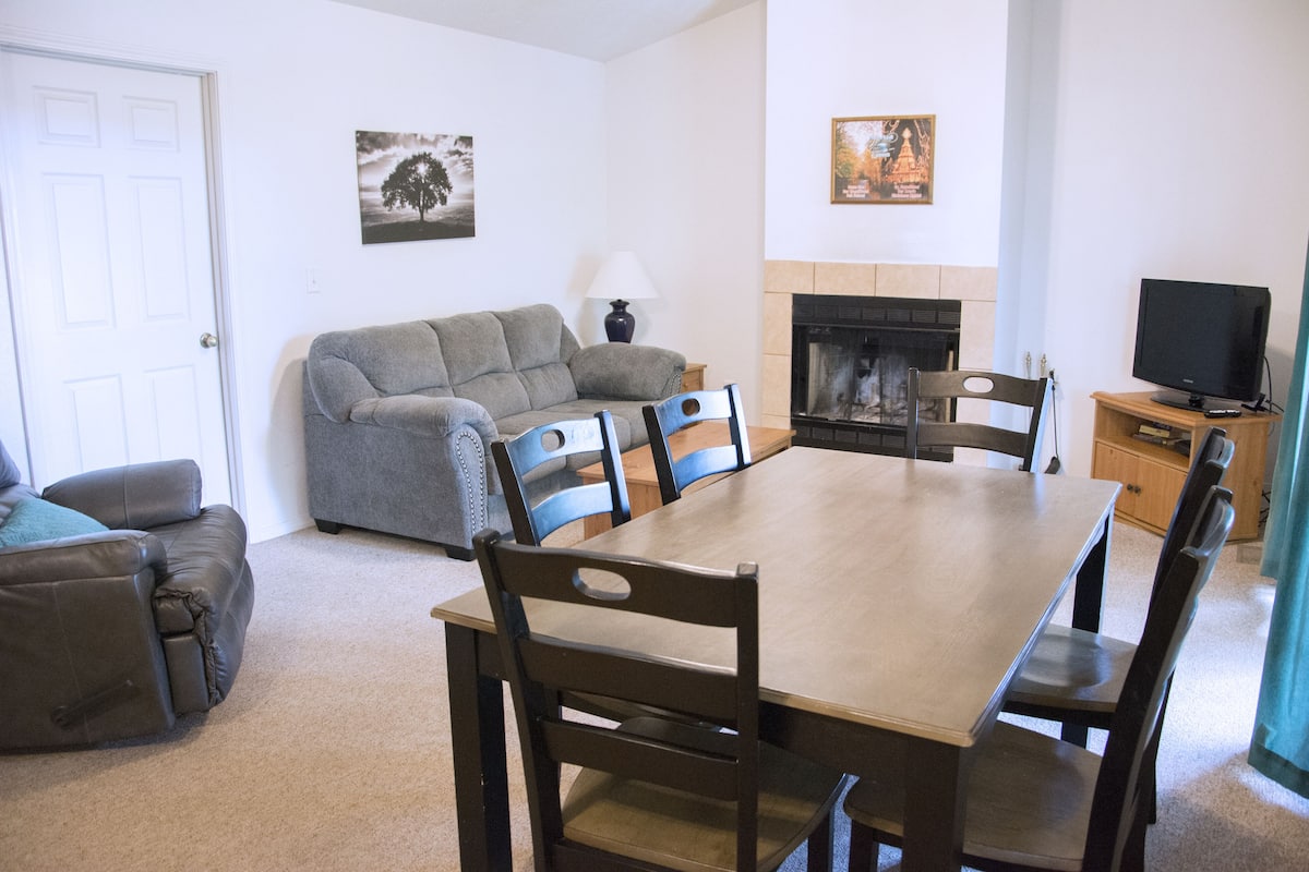 Uma sala de estar com sofá, mesa de jantar com cadeiras, lareira e televisão.