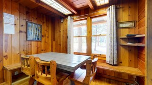 A wooden cabin with a dining table, chairs, and a bench. There are windows with curtains, a framed picture on the wall, and a shelf with books. - Spacious and Lovely Mountain Retreat (Bayfield)