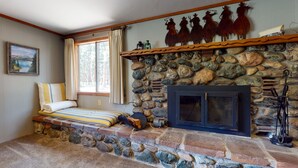 A cozy room with a stone fireplace, a bed with striped bedding, and a window with curtains. - Spacious and Lovely Mountain Retreat (Bayfield)
