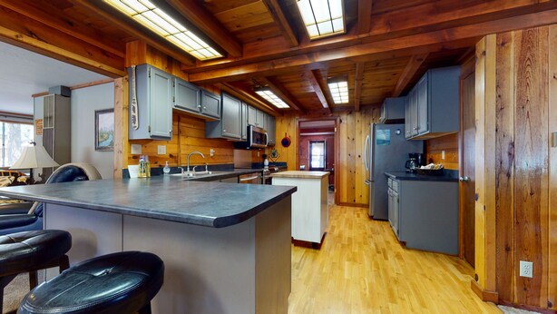 A modern kitchen with wooden beams, a central island, bar stools, and a refrigerator. - Spacious and Lovely Mountain Retreat (Bayfield)