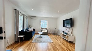 Un salon spacieux doté d’un plancher en bois franc, d’un ensemble de canapés, d’une table basse et d’un téléviseur fixé au mur.