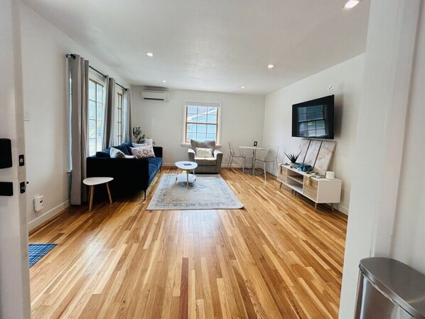 A spacious living room with hardwood flooring, a sofa set, a coffee table, and a TV mounted on the wall.