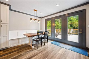A dining area with a wooden table and chairs, a hanging light fixture, and a view of the outdoors through large sliding doors.