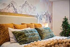 A bed with multiple pillows, a headboard, and a wall with a mountain painting.