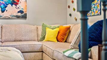 Un canapé d’angle beige, agrémenté d’un plaid vert en tricot, d’un coussin jaune et d’un coussin orange.