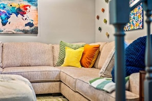 A beige sectional sofa with a green knitted throw, a yellow pillow, and an orange pillow.