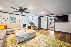 A living room with a sectional sofa, a ceiling fan, a staircase, and a flat-screen TV mounted on the wall.