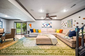 A modern living room with a sectional sofa, a dining area, and a staircase. - Red’s Luxury Retreat; 4bd 3.5 ba, 2300 sq ft (Peoria)