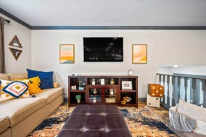 A living room with a sofa, ottoman, and a wooden cabinet with decorative items. - Red’s Luxury Retreat; 4bd 3.5 ba, 2300 sq ft (Peoria)