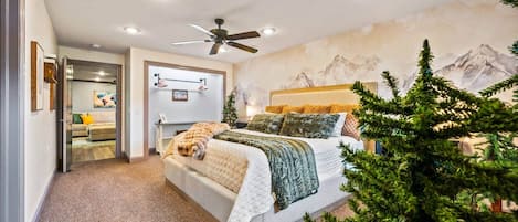 Quarto com cama, ventoinha no teto, escrivaninha fixada na parede e um mural de montanhas.