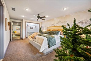 A bedroom with a bed, a ceiling fan, a wall-mounted desk, and a mountain mural.