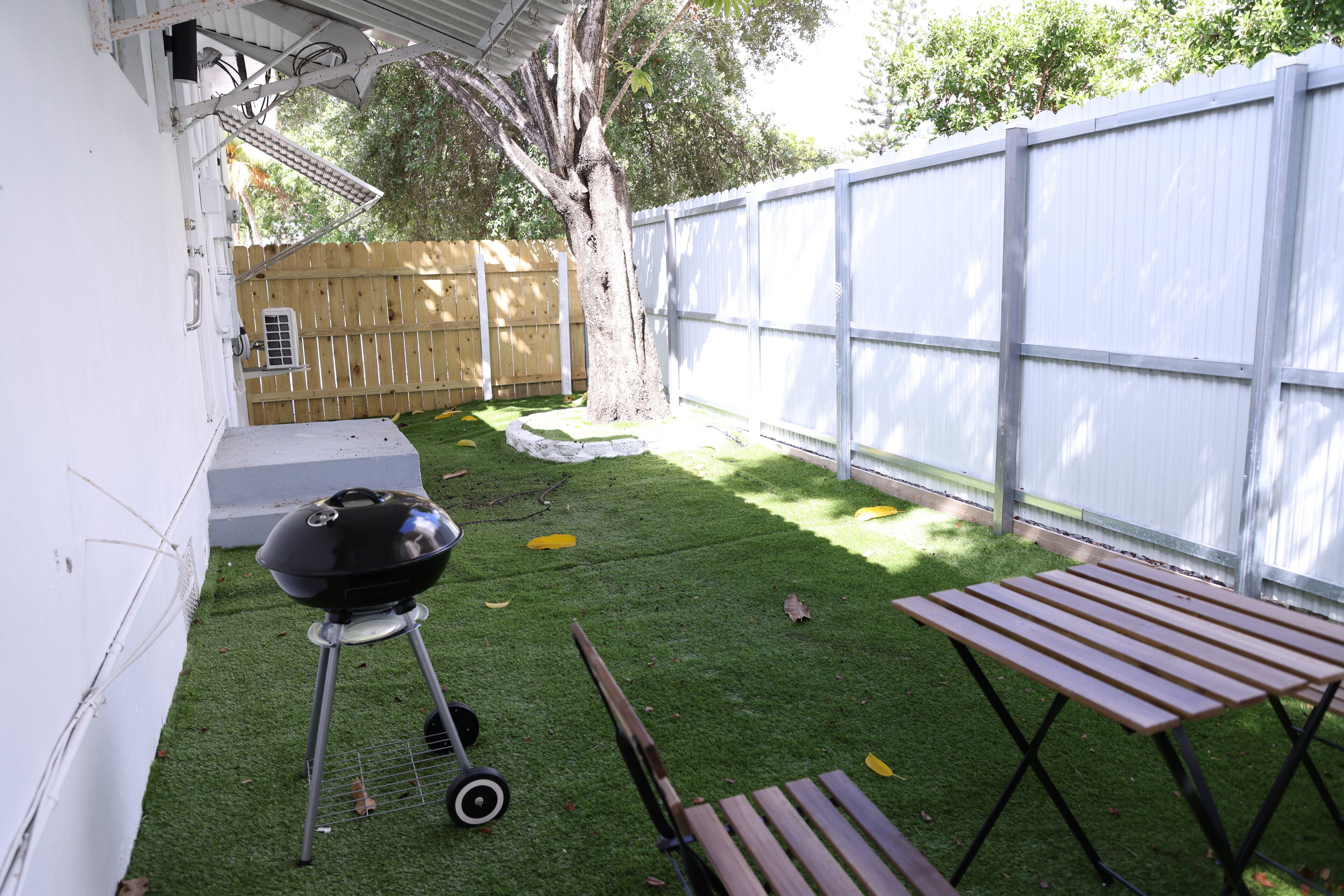 Ein Garten mit künstlichem Rasen, einem Holztisch, einem Grill und einem Holzzaun.