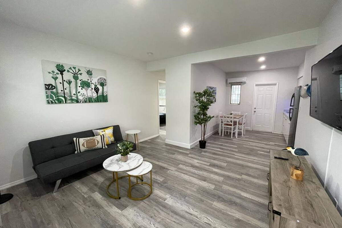 A modern living room with a grey sofa, two white round tables, and a dining area with a white table and chairs.