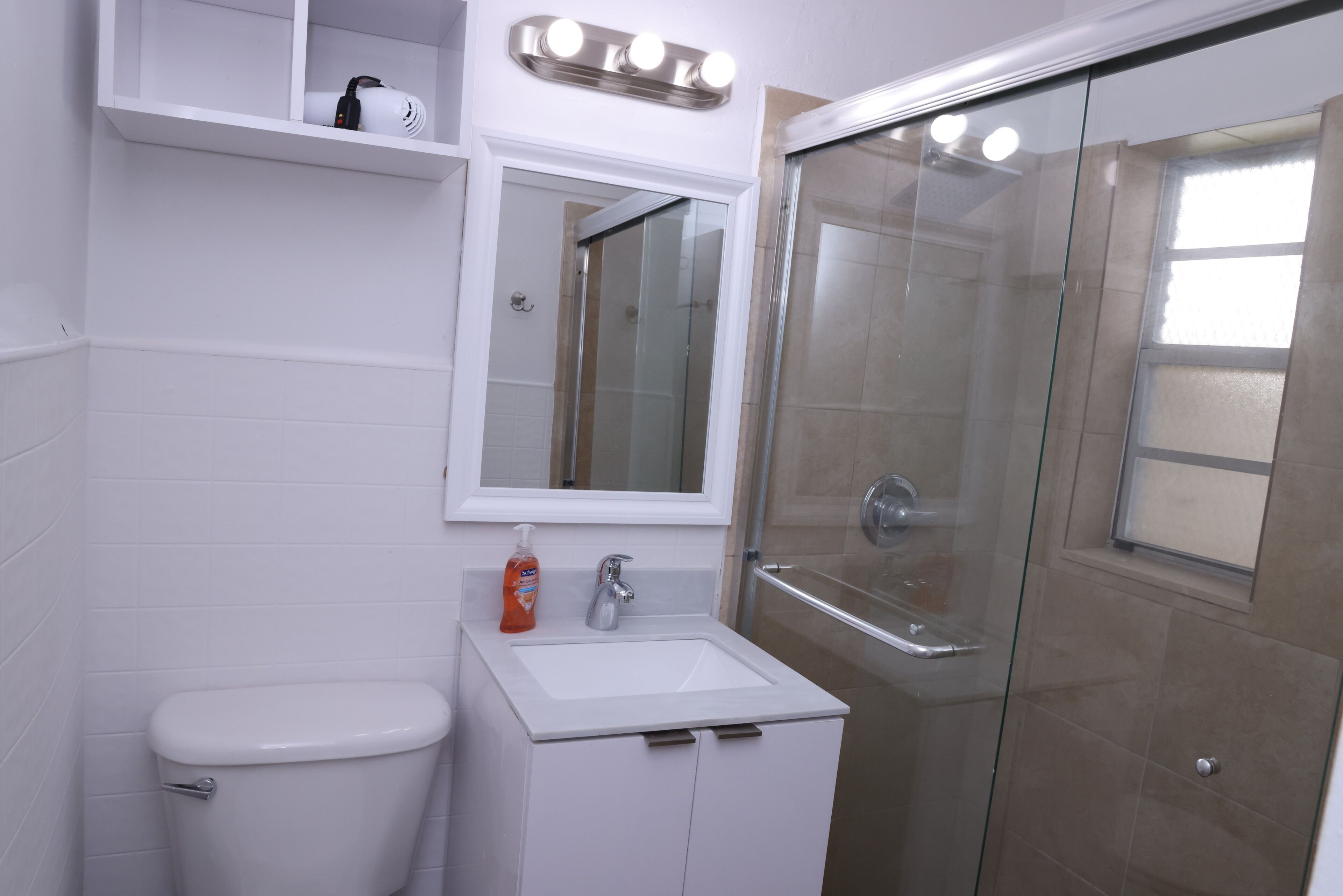 A bathroom with a toilet, sink, mirror, and glass-enclosed shower.