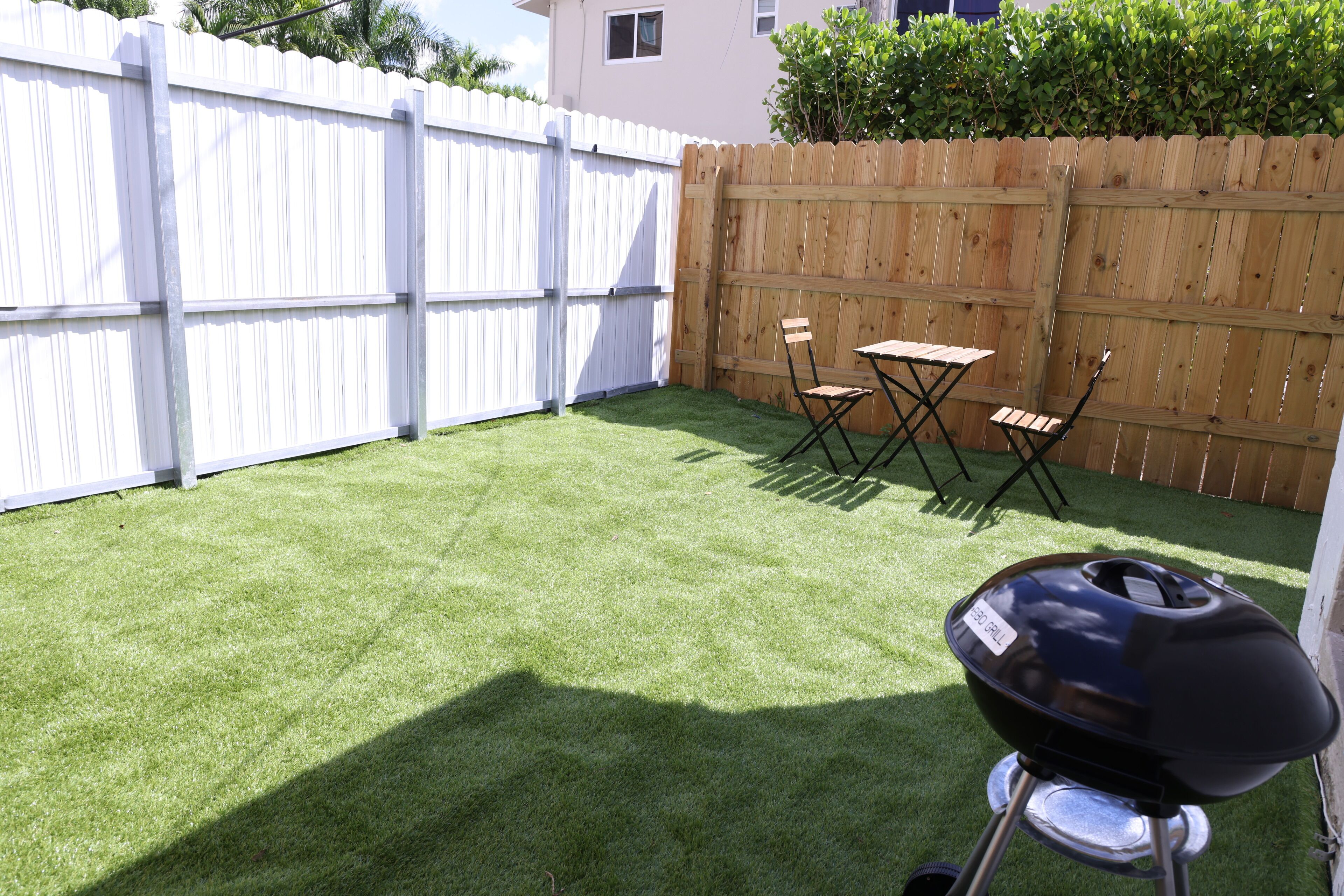 A backyard with artificial grass, a wooden fence, and a barbecue grill.