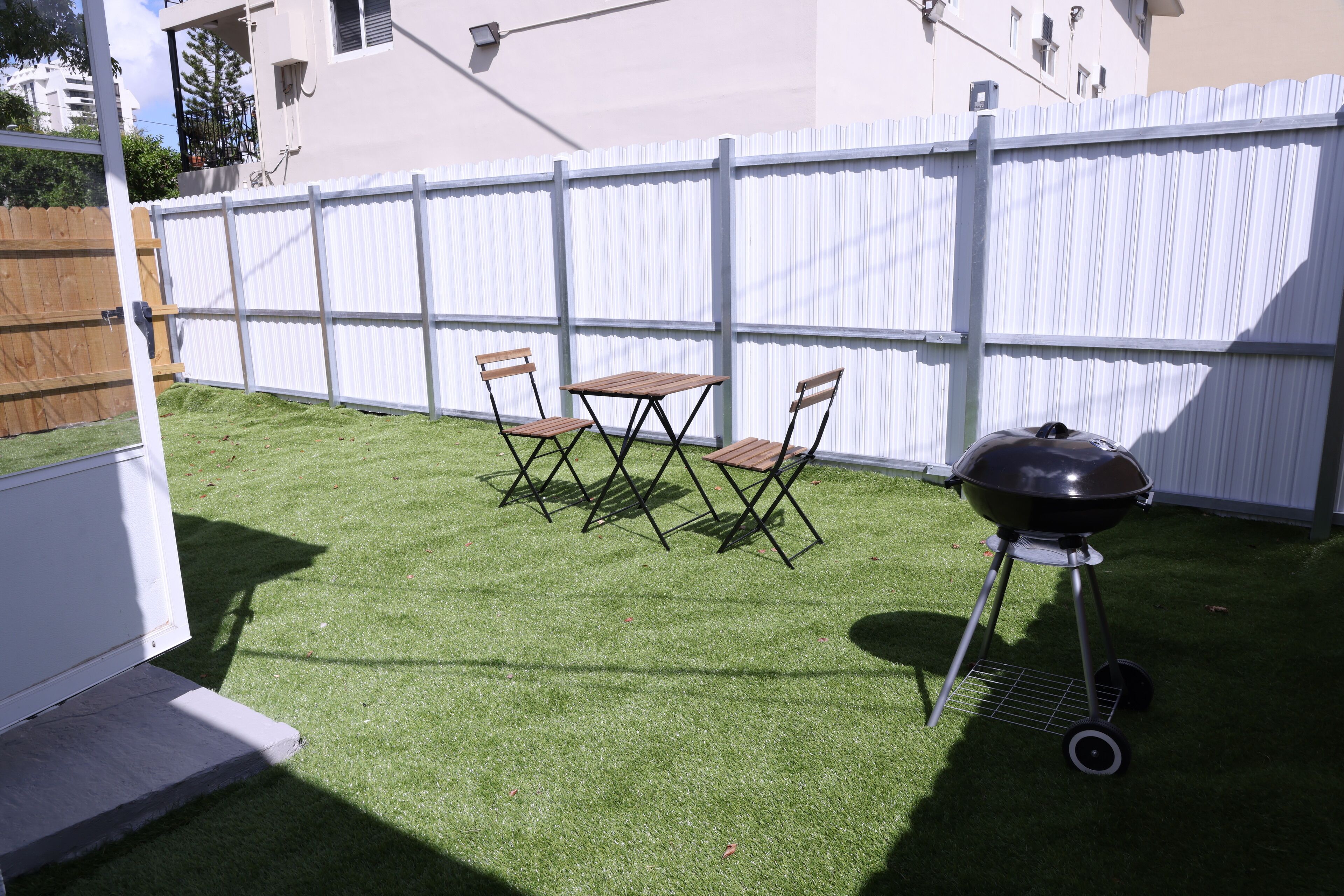A backyard with artificial grass, a barbecue grill, and two folding chairs.
