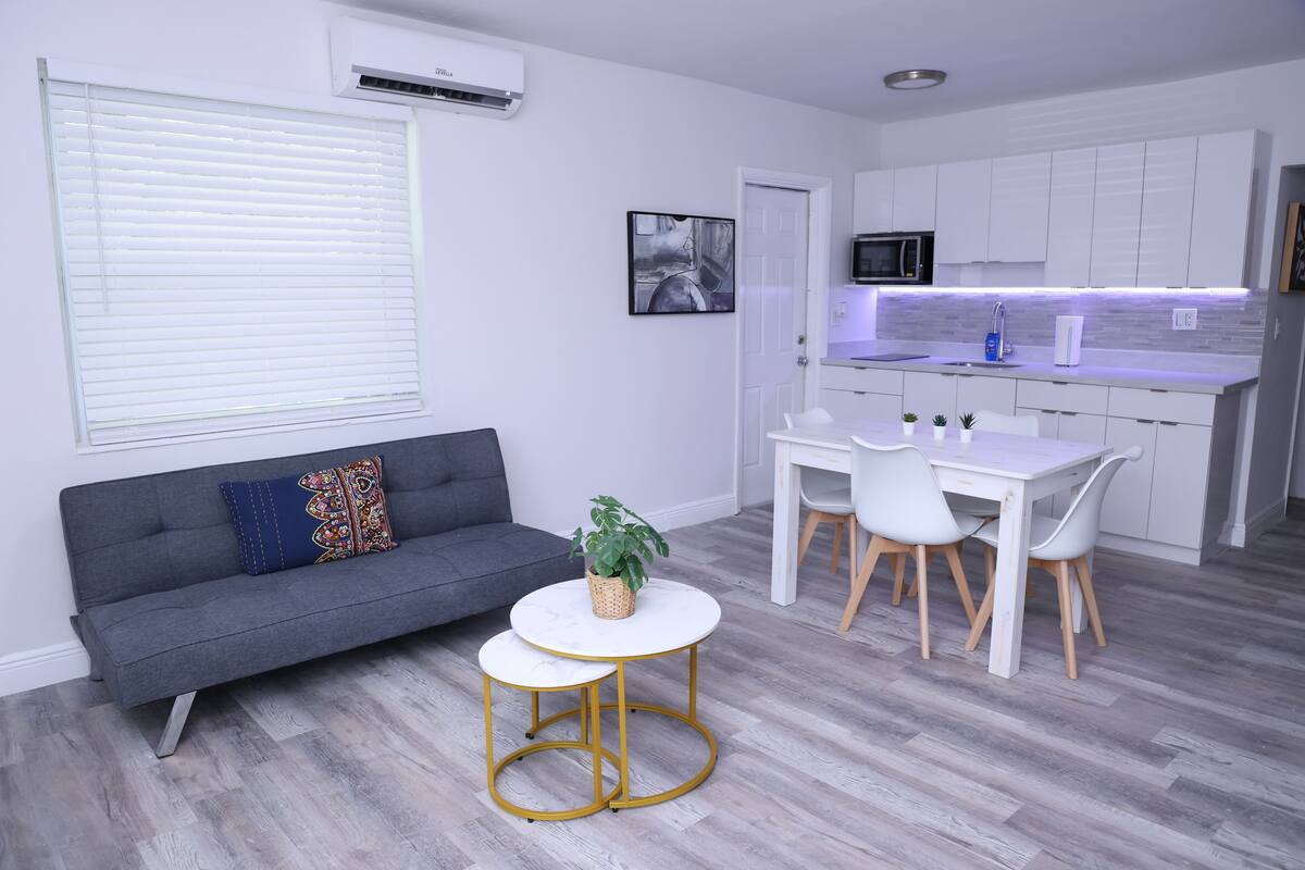 A modern living room with a grey sofa, a small round table, and a white dining table with chairs.
