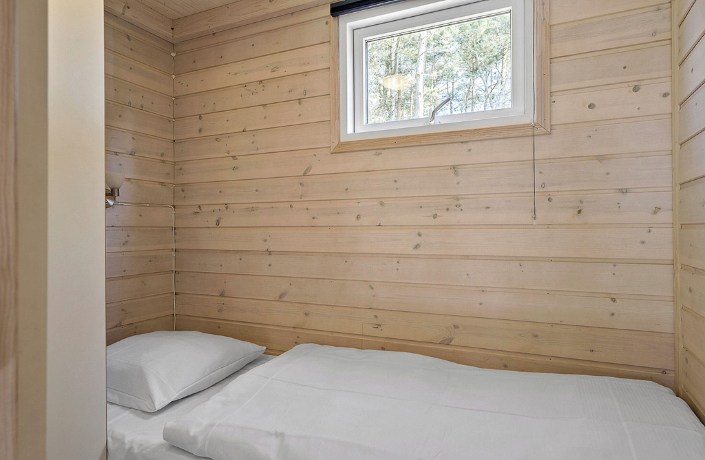Une petite cabine avec un lit simple, des murs en bois et une fenêtre.