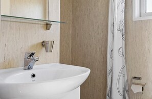 A bathroom with a white sink, a glass shelf, a towel rack, and a shower curtain.