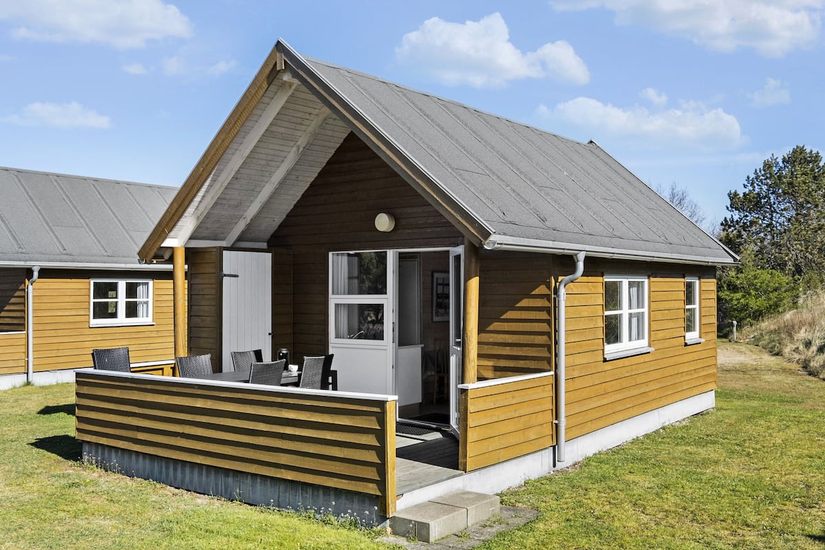 A wooden cabin with a pitched roof, a porch with seating, and a small deck area.
