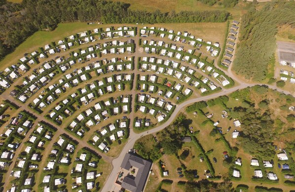 An aerial view of a campground with multiple RV and tent sites arranged in a semi-circular pattern.
