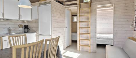 A compact, wooden cabin with a kitchenette, a dining area with a table and chairs, a ladder leading to a loft bedroom, and a small window.