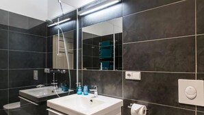 Une salle de bain moderne avec des carreaux foncés, un lavabo blanc, un miroir et une douche.