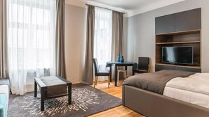 Une chambre d’hôtel moderne équipée d’un lit, d’un téléviseur fixé au mur, d’une petite table avec des chaises et d’un bureau avec un ordinateur.