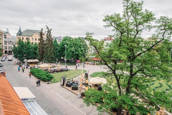 Une place publique agrémentée d’arbres, de sièges extérieurs et d’une rue pavée.