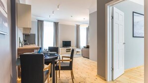 Ein modernes Wohnzimmer mit Essbereich, einem Fernseher und einer Tür zu einem weiteren Raum.