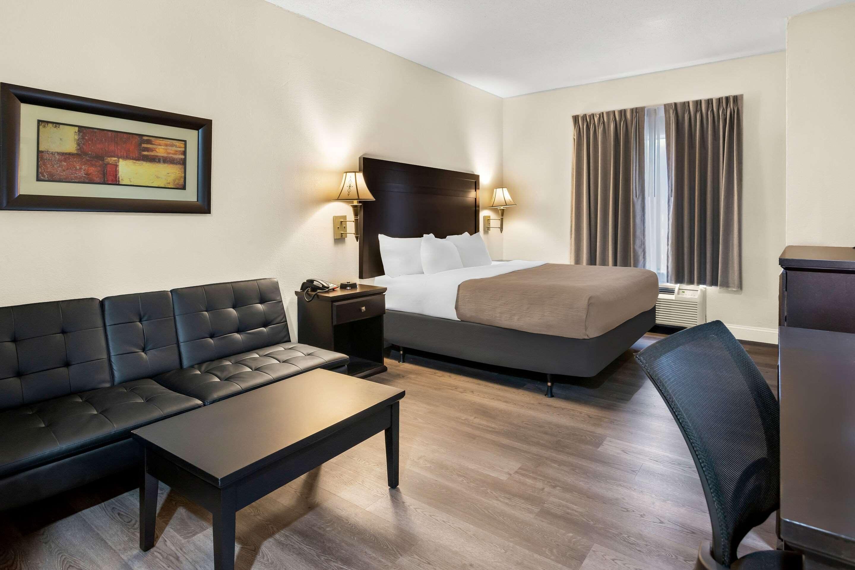 Una habitación de hotel con una cama, un sofá, una mesa, una silla y un cuadro en la pared.