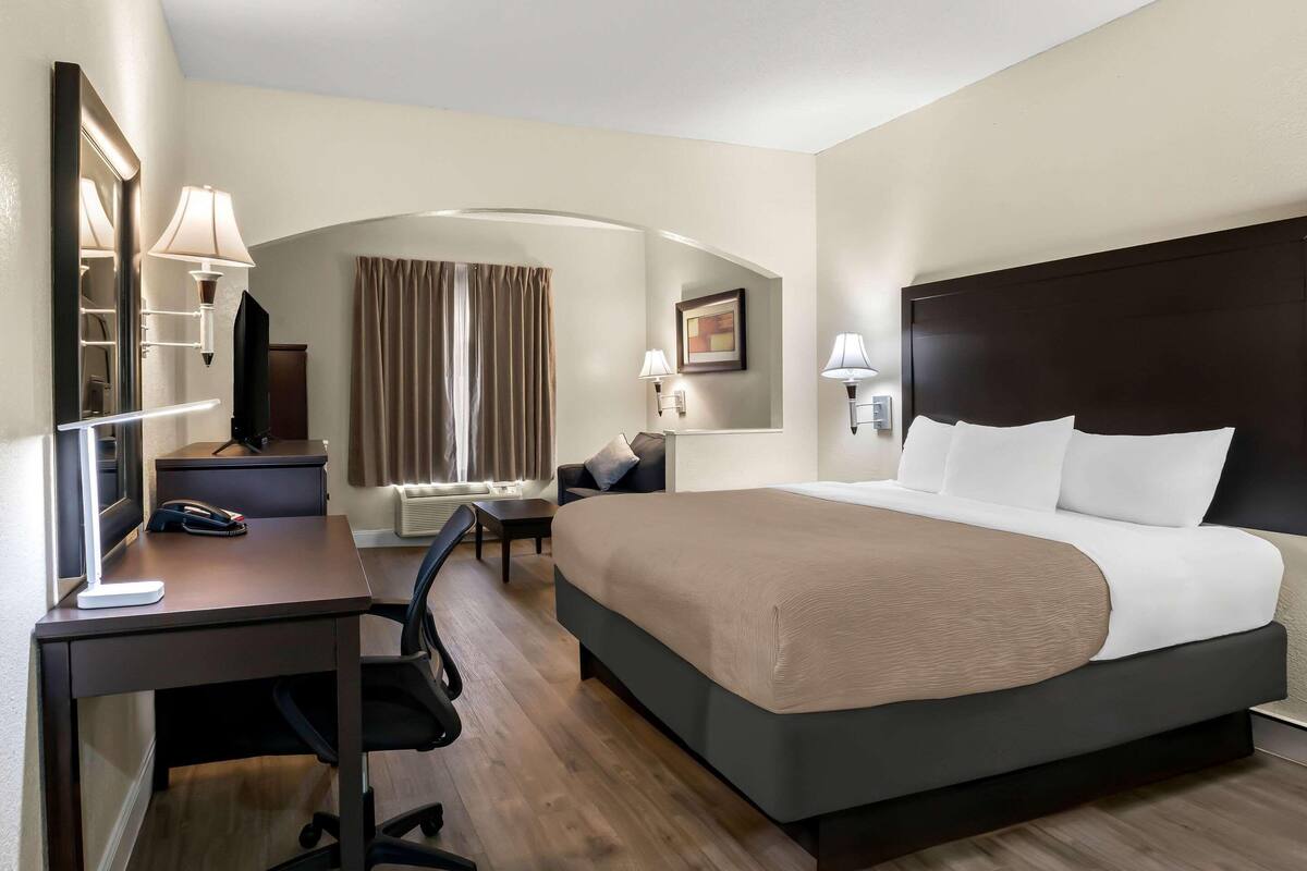 A hotel room with a bed, desk, chair, and a TV.