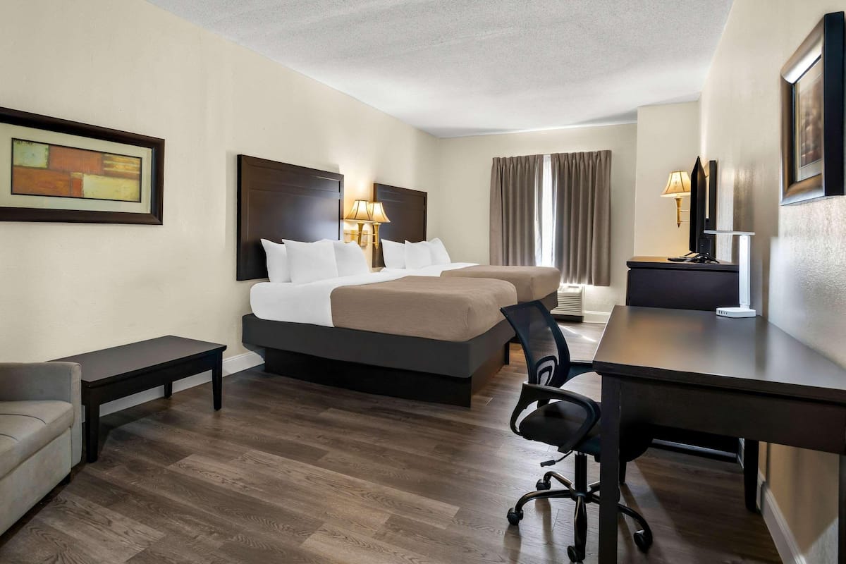 A hotel room with a bed, two bedside tables, a desk, a chair, a TV, and a painting on the wall.