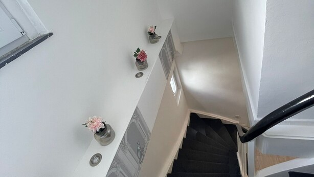 Una scala con corrimano, un muro bianco con elementi decorativi e una porta in cima.