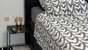 Camera da letto con una testiera nera, una coperta a motivi, una lampada da comodino e un comodino nero con un telecomando.