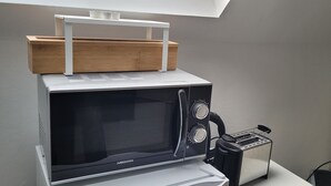 Un forno a microonde con una scatola di legno sopra, un tostapane e uno scaffale bianco.