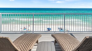 Une vue sur la plage depuis un balcon agrémenté de meubles en osier et d’une balustrade.