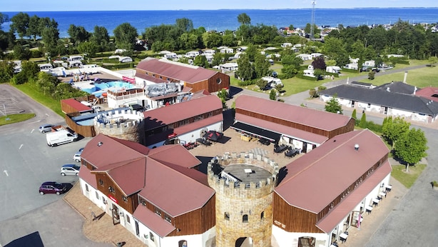 A resort with a central courtyard, multiple buildings with red roofs, and a large body of water in the background. - First Camp Hasmark Strand Fyn (Otterup)