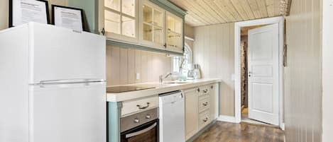 A kitchen with a white refrigerator, wooden cabinets, a built-in oven, and a wooden floor.