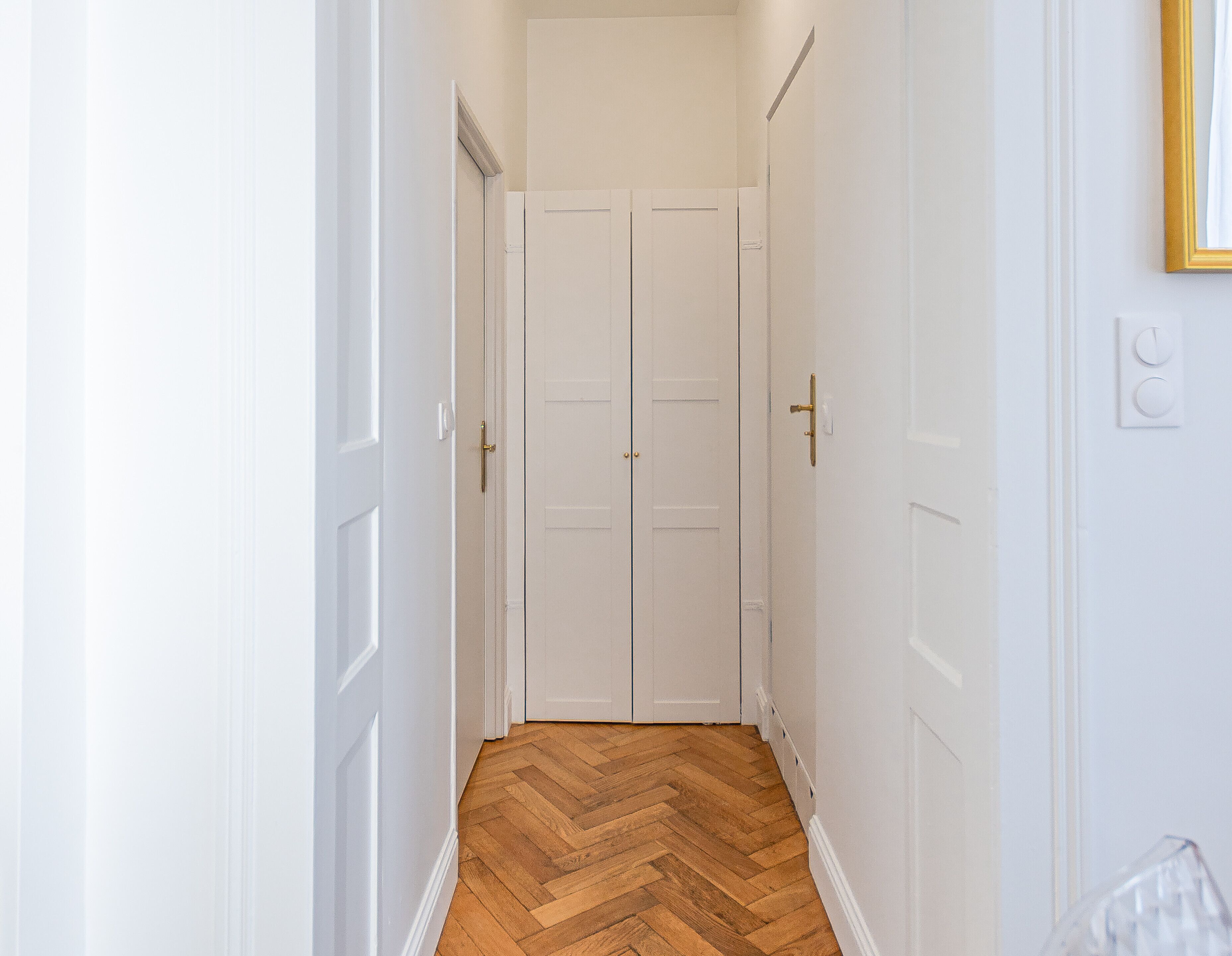 Un pasillo con puertas blancas y un suelo de madera en espiga.